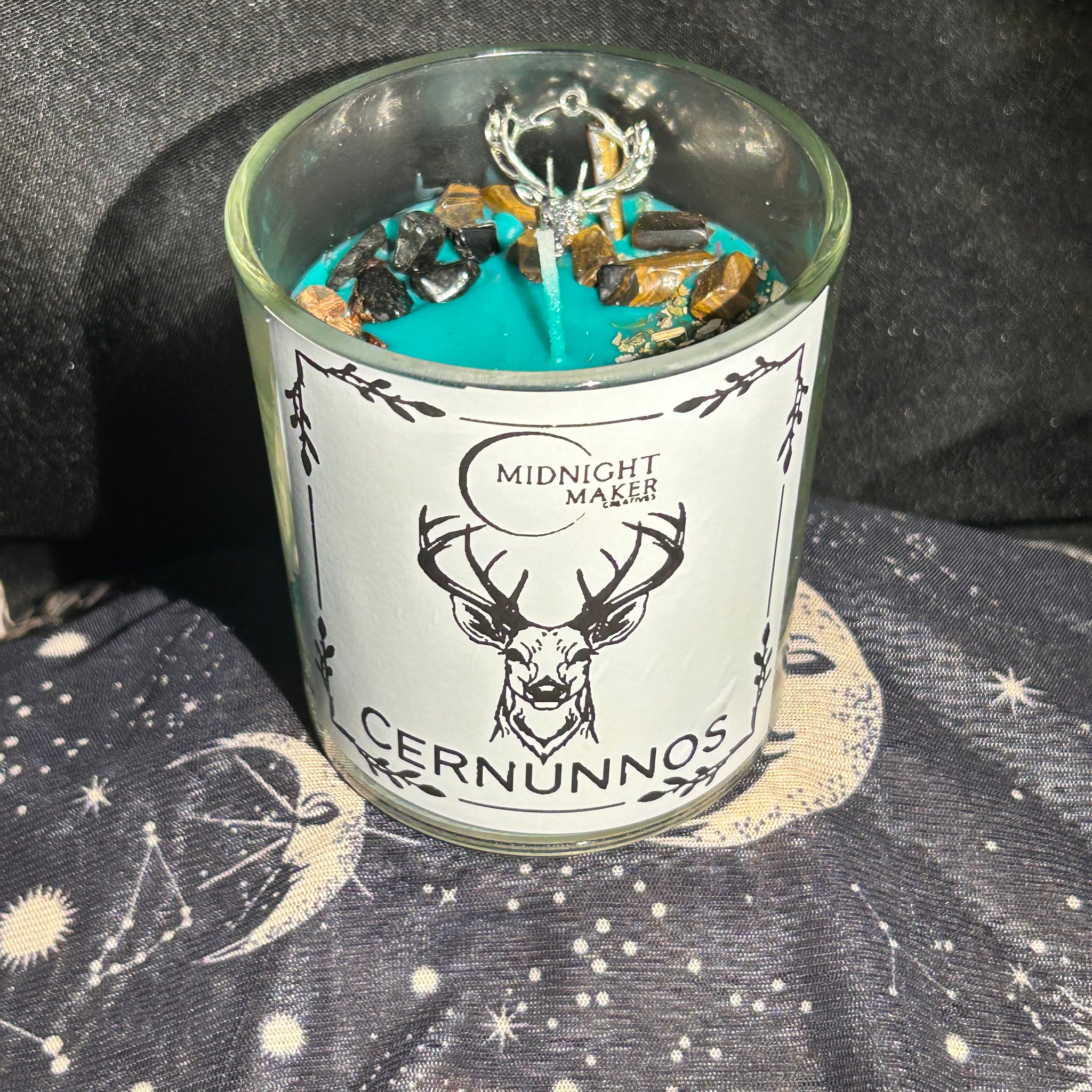 Glass votive candle with a green candle dressed with black tourmaline and tigers eye crystal chips, oak and mugwort and a deer head charm