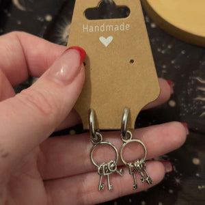 Hand holding Keeper of keys, stainless steel silver hooped earrings adorned with 3 keys per earring to honour the goddess Hekate. 