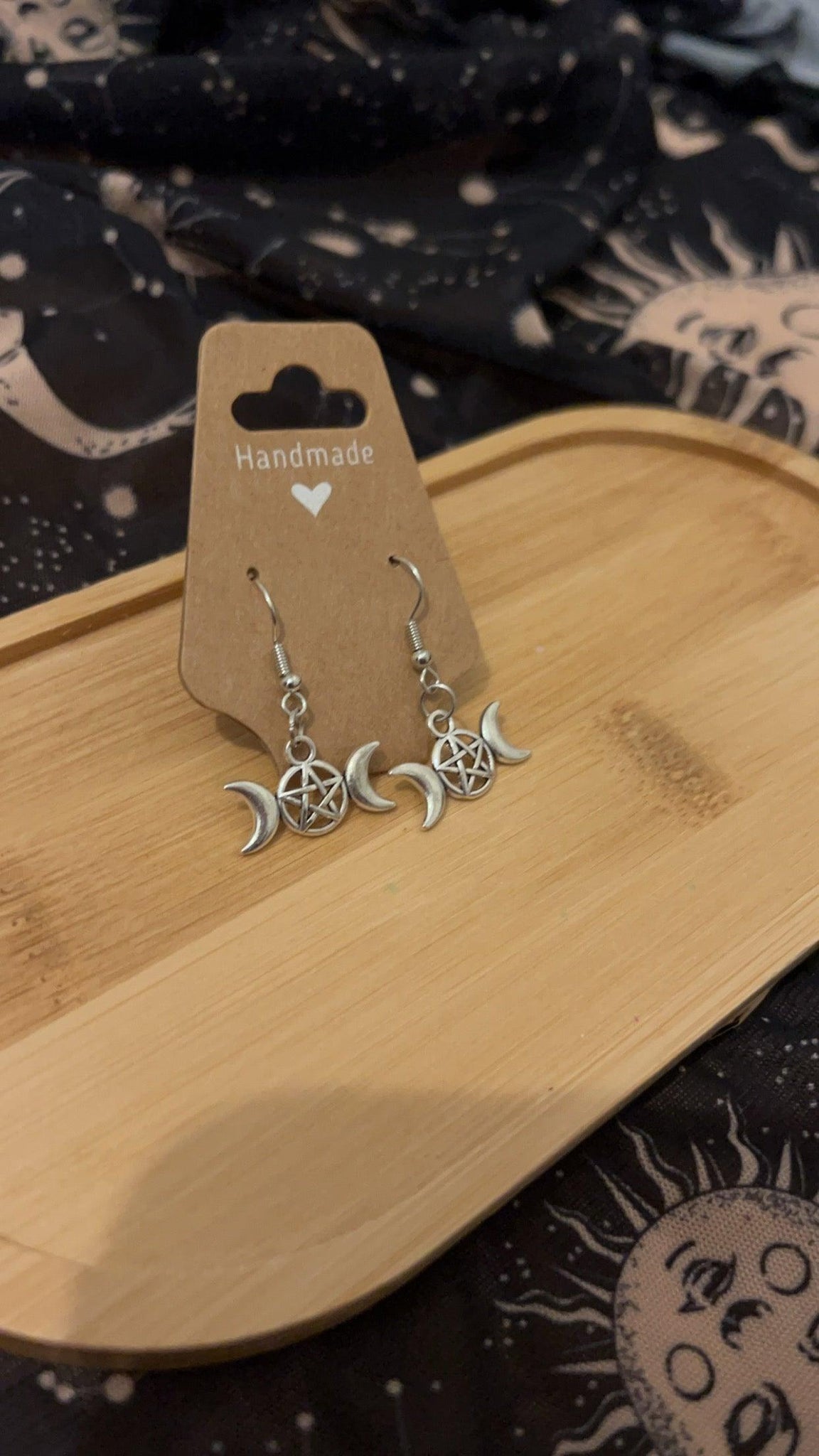 Side angle photo of Drop style silver earrings adorned with triple moon goddess symbol with a pentacle in the middle of the full moon. 